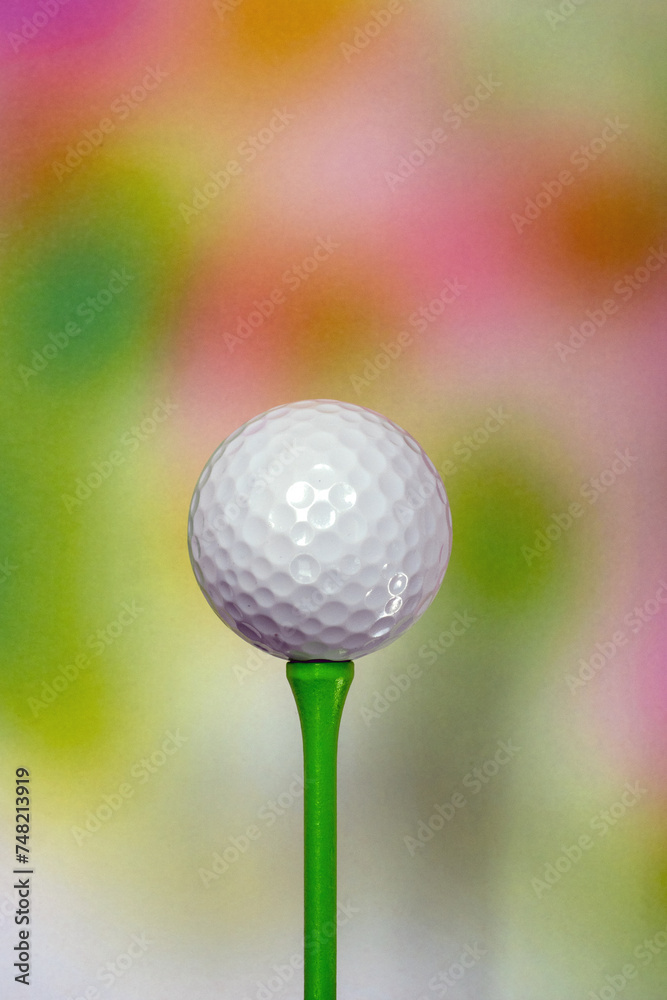 A plain white unbranded golf ball on a coloured 70mm tee peg in front of a multi-coloured background A plain white unbranded golf ball on a coloured 70mm tee peg in front of a multi-coloured background