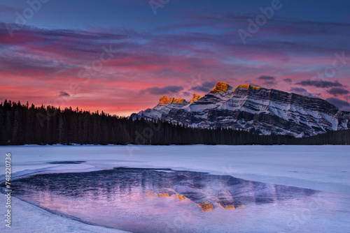 Golden sunrise at Two Jack Lake in Banff with alpenglow Rundle Mountain peaks reflecting off frozen lake