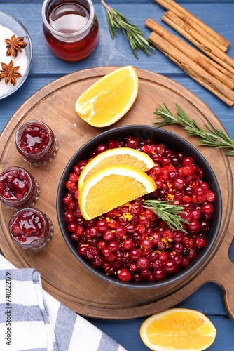 Cranberries in bowl, jars with sauce and ingredients on blue wooden table, flat lay