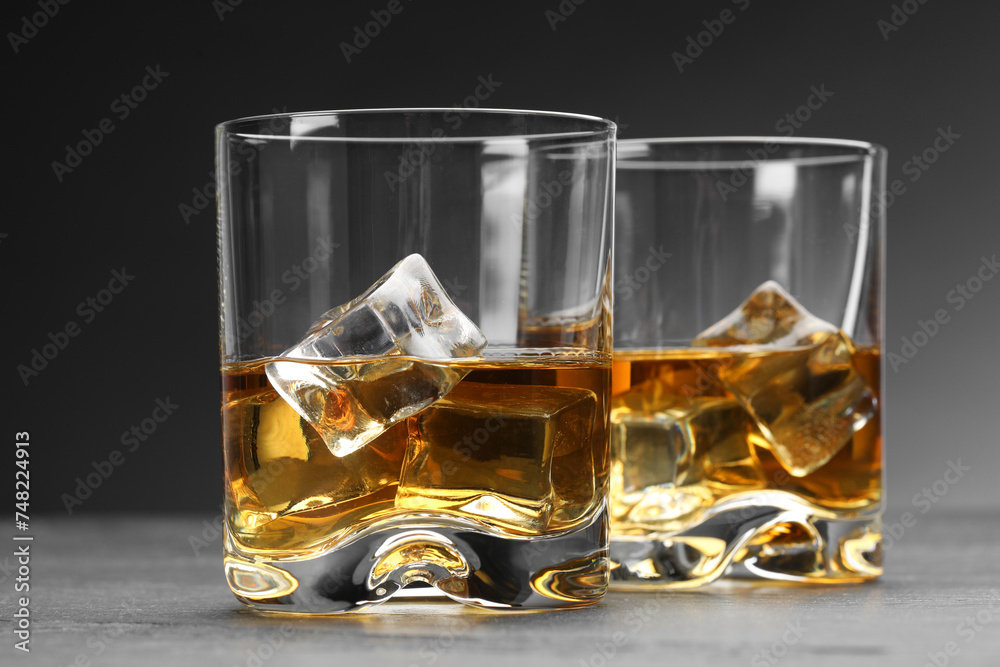 Whiskey and ice cubes in glasses on grey table, closeup