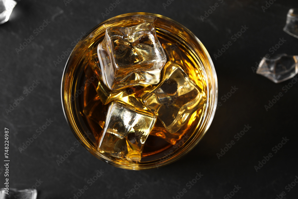 Whiskey and ice cubes in glass on black table, top view