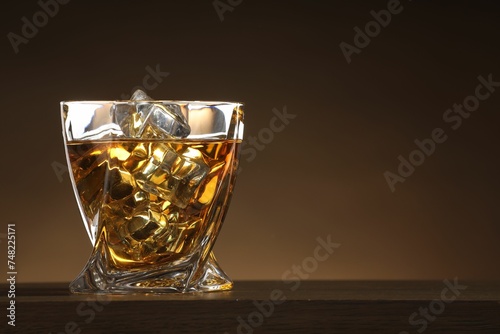 Whiskey with ice cubes in glass on table against brown background. Space for text