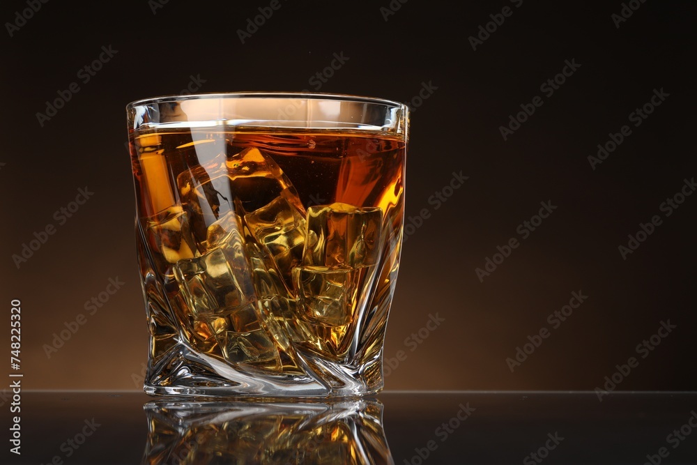 Whiskey with ice cubes in glass on table against color background, space for text