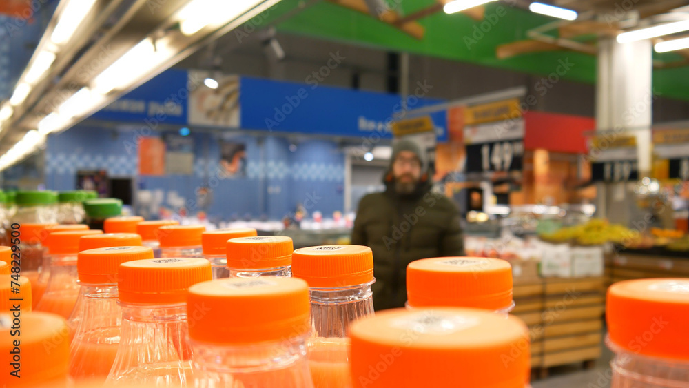 Close-up of many bottles of juice in a grocery store and a buyer is heading towards them - obrazy, fototapety, plakaty 