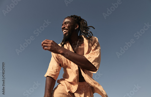 Cheerful young black man standing and looking away under blue sky