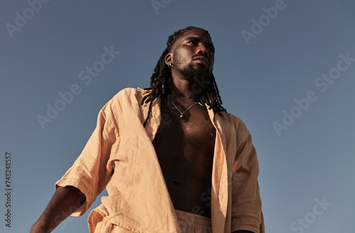 Young black man standing and looking away under blue sky