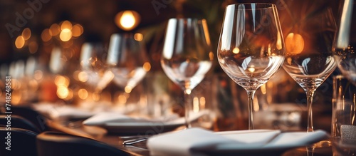 A row of empty wine glasses neatly arranged on top of a dining table, set for a dinner service in a restaurant. The crystal clear glasses reflect the ambient light,