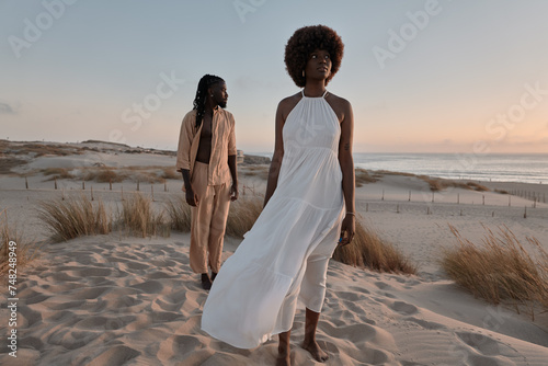 Black couple standing away on sand with dry grass plants in evening light