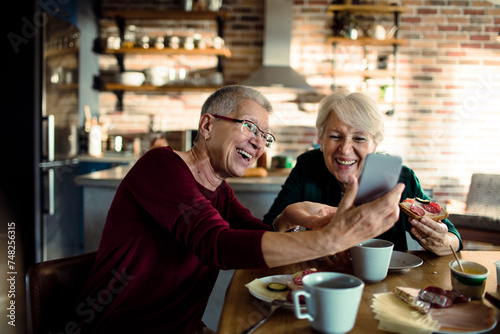 Two senior women using smartphone together at kitchen table