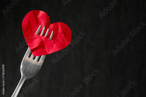 Broken heart. Red paper heart pierced with fork against black background, closeup. Space for text