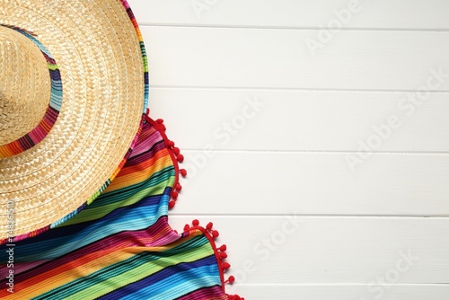 Mexican sombrero hat and colorful poncho on white wooden background, flat lay. Space for text