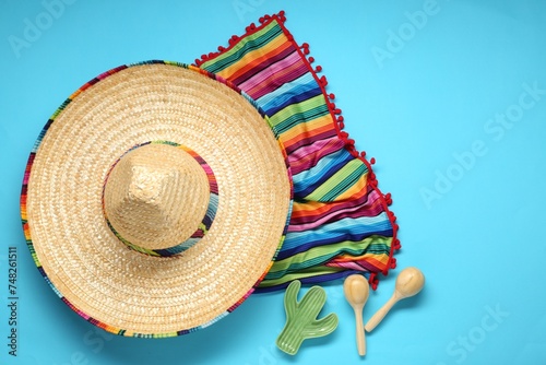 Mexican sombrero hat  maracas  toy cactus and colorful poncho on light blue background  flat lay. Space for text