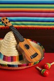 Mexican sombrero hat, ukulele and maracas on red table