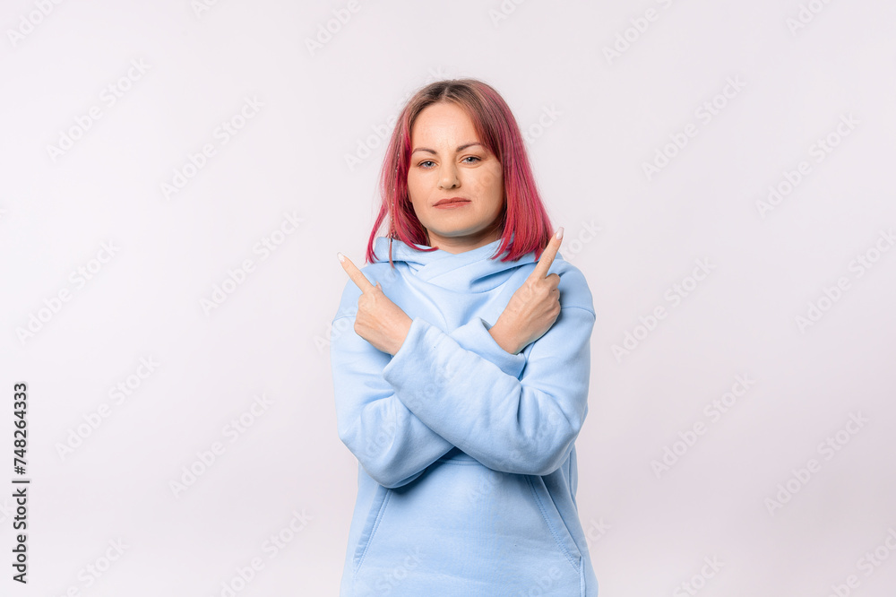 Confused young woman pointing sideways, looking clueless, puzzled to choose. Lovely female model with pink hair in a blue hoodie standing over white background Confused young woman pointing sideways, looking clueless, puzzled to choose. Lovely female model with pink hair in a blue hoodie standing over white background