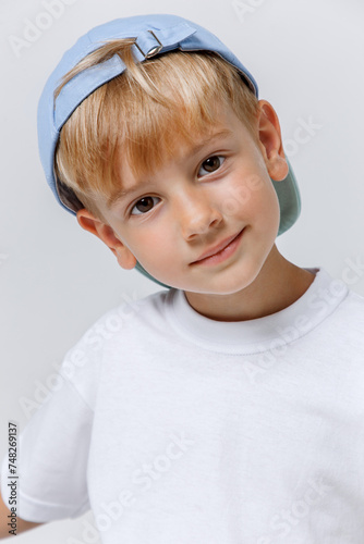 Close-up portrait od little blonde boy in baseball cap and white t-shirt on white background