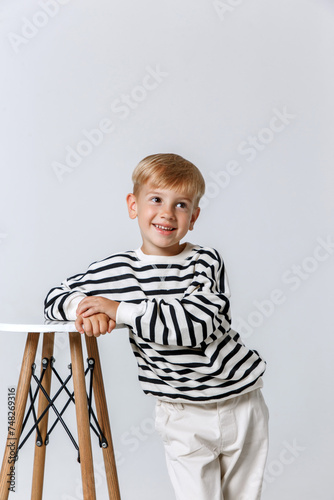 Little smiling kid boy in striped sweatshirt and white trousers posing at studio as a fashion model.