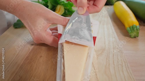 Chef opens a package of Parmesan cheese, wooden dock, vegetables in the background, home cooking. Close-up, side view