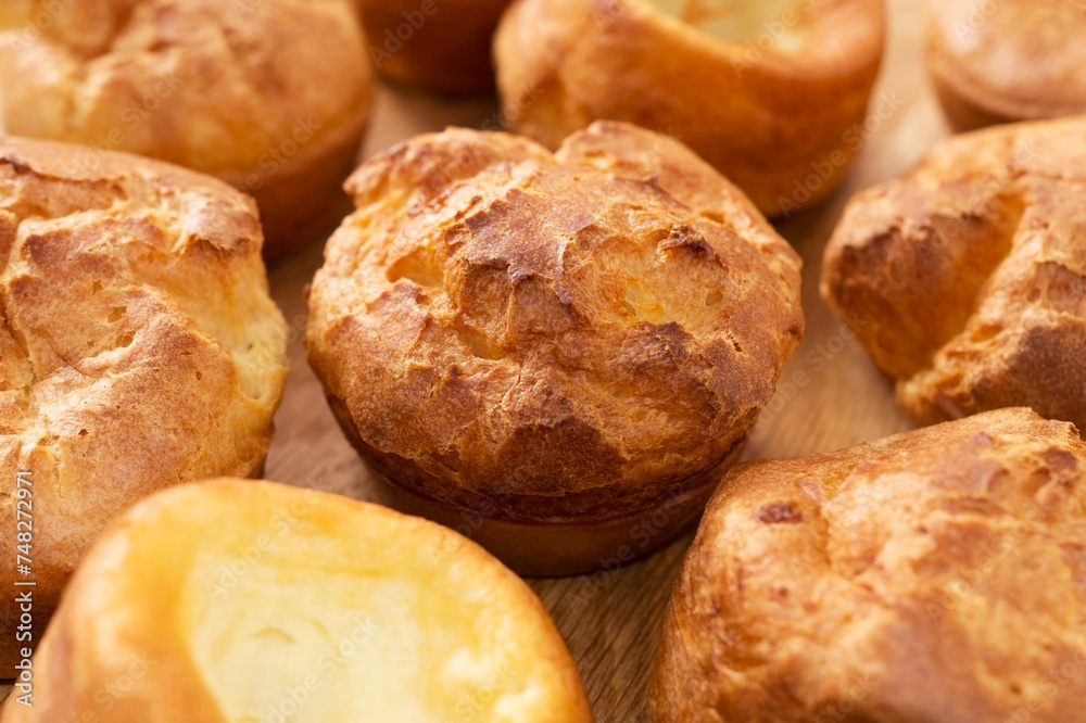 A lot of fresh hot popovers on wood plate or wooden board. Easy cooking, tasty breakfast, close up. Yorkshire pudding