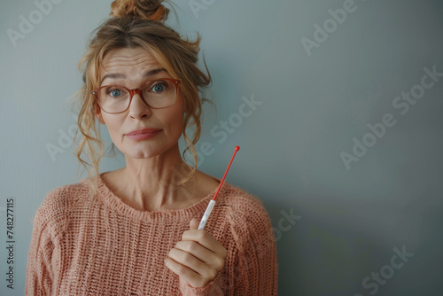 Nervous caucasian middle-aged woman holding pregnancy test holding hand on belly, unsure about her pregnancy and future, looking at the camera with a anxious expression. Health care, fertility, family photo