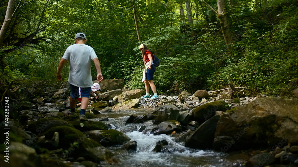 Family of mother and two boys jumping rocks across creek. Creative. Young travelers hiking together in North Carolina woods.