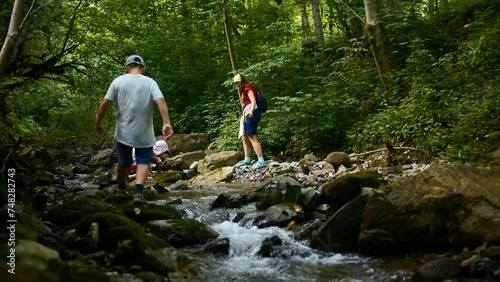 Family of mother and two boys jumping rocks across creek. Creative. Young travelers hiking together in North Carolina woods.