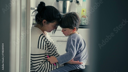 Candid mother explaining child's misbehaviour in caring warm embrace after getting hurt in tender authentic genuine loving scene at kitchen, parental guidance