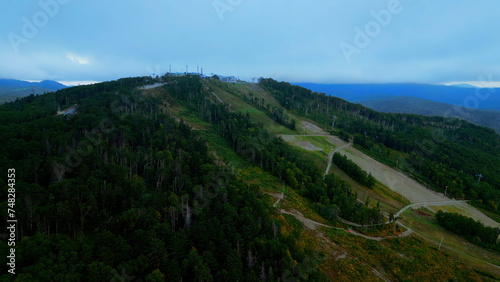 Aerial view of cable cars in mountains. Clip. Travel and outdoor activities, hills, coniferous trees and blue sky.