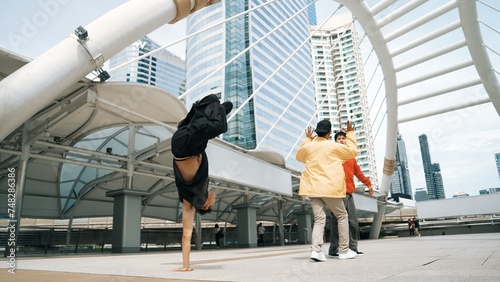 Group of professional happy street dancer cheer up while asian hipster perform b boy dance at urban city surrounded by people with low angle camera. Break dance concept. Outdoor sport 2024. Sprightly.