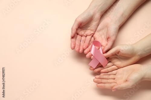 Fototapeta Naklejka Na Ścianę i Meble -  Breast cancer awareness. Women holding pink ribbon on beige background, top view. Space for text