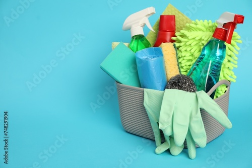 Different cleaning products in basket on light blue background, space for text