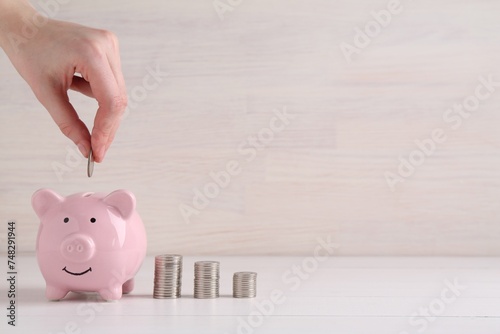 Financial savings. Woman putting coin into piggy bank at white wooden table, closeup. Space for text
