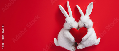 Dois coelhos brancos com coração vermelho sobre fundo vermelho. Conceito de dia dos namorados photo