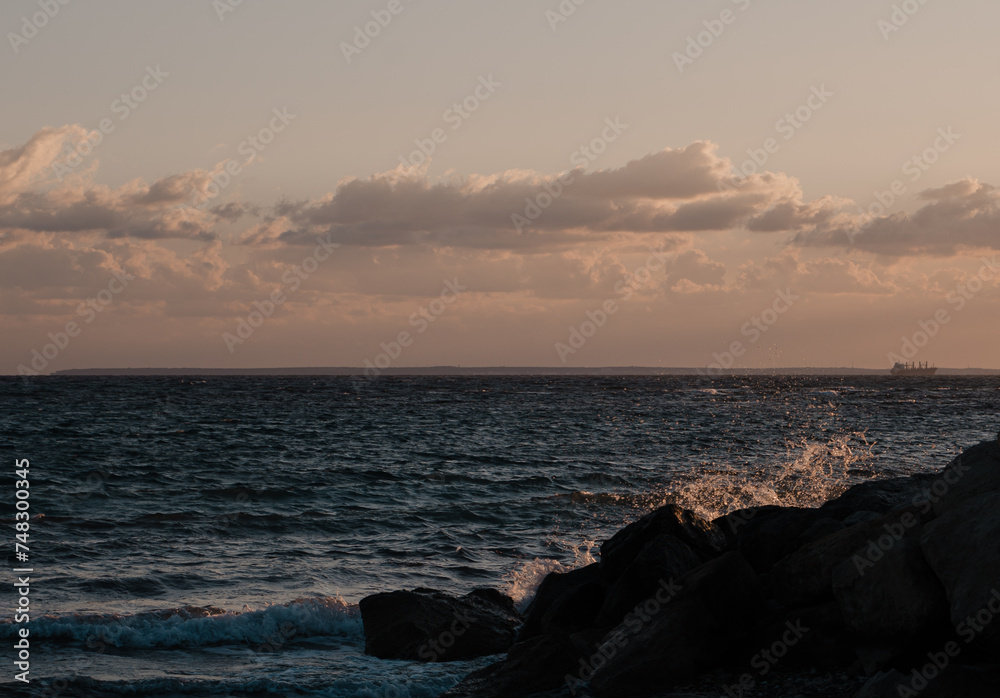 Fototapeta premium sunset on the beach with crashing waves on the rocks with ship on the horizon 
