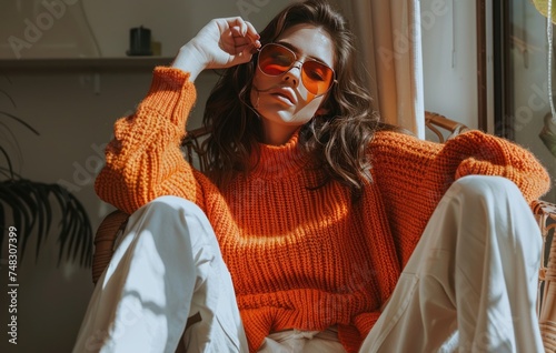 A woman sitting on a chair in an orange sweater and white pants