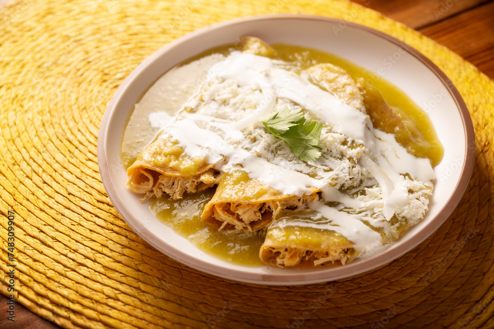Green enchiladas. Typical Mexican dish made with a folded or rolled corn tortilla filled with shredded chicken and covered with spicy green sauce, cream, grated cheese and onion. Green enchiladas. Typical Mexican dish made with a folded or rolled corn tortilla filled with shredded chicken and covered with spicy green sauce, cream, grated cheese and onion.