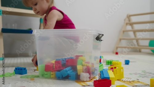 The child himself cleans up toys in the nursery after the game. Toddler baby collects toys in a box. Kid girl aged 2,5 year old.