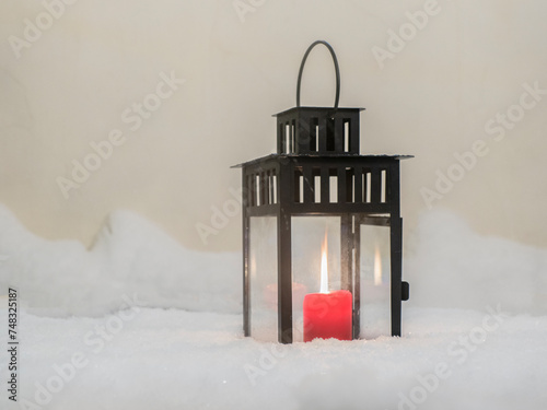 Burning red Christmas candle on fresh snow background,  lantern in snow on the table snow covered