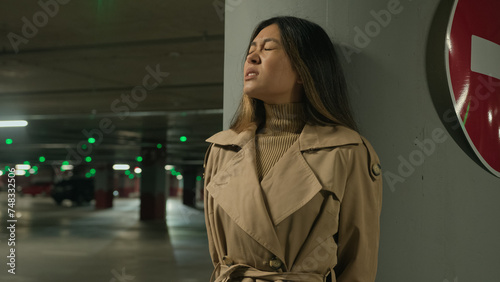 Frightened Asian ethnic chinese korean woman hiding from danger pursuit threat phobia in underground shelter night dark car parking scared fearful girl stand alone near stop driving traffic road sign photo