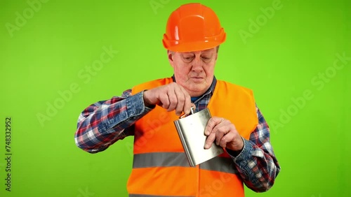 Worker looks around and drinks alcohol from flask. photo