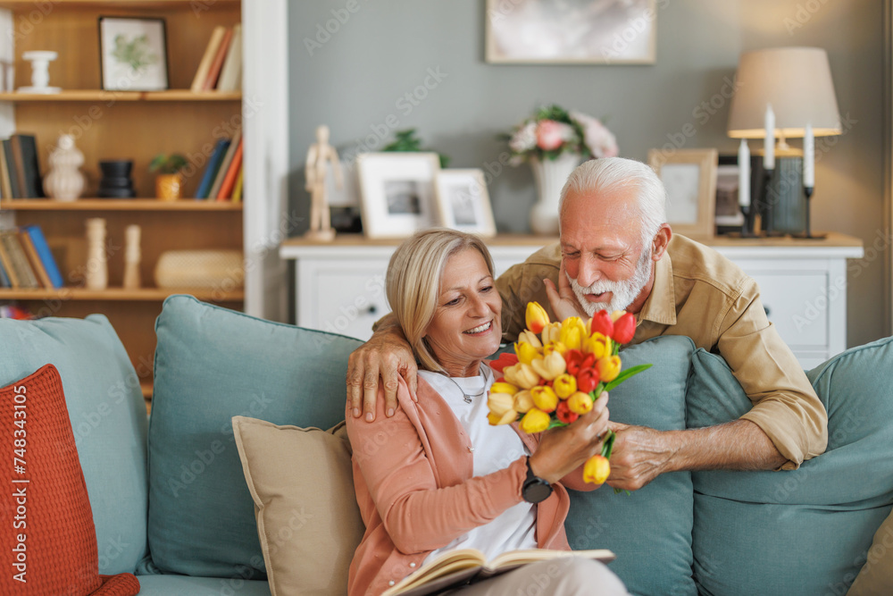 Anniversary surprise - Senior man presents flowers to his wife at home - obrazy, fototapety, plakaty 
