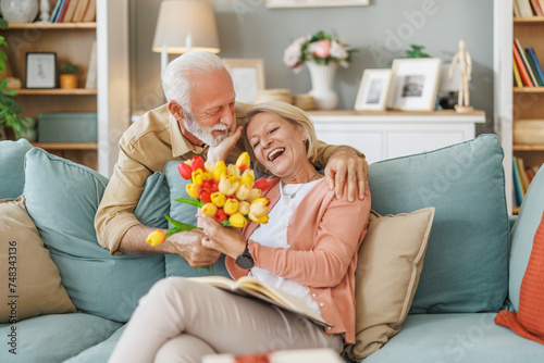 Anniversary surprise - Senior man presents flowers to his wife at home