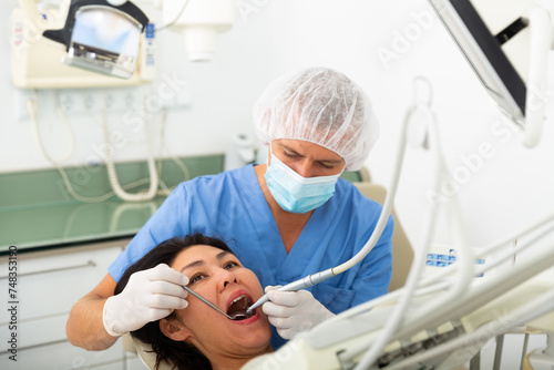 Practitioner male dentist drilling tooth to asian female patient in dental studio