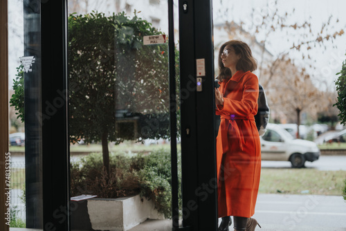 A thoughtful woman in business attire examines the cloudy outdoors through a glass door. Her contemplative stance suggests a moment of decision or reflection.