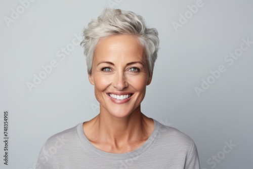 Portrait of a smiling senior woman with short grey hair standing against grey background
