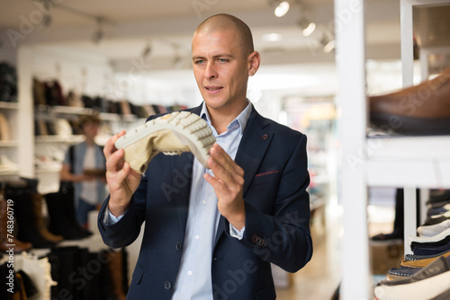 Interested bald man choosing new comfortable shoes in store, checking softness of sole of moccasins photo