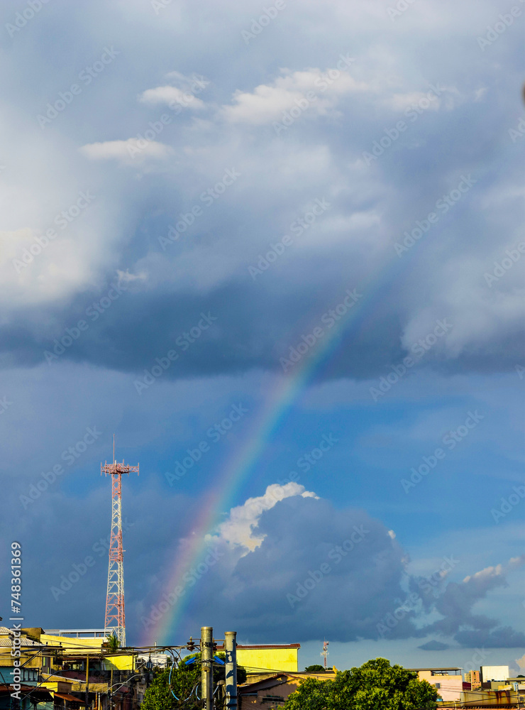 Beautiful sky with dark clouds and rainbow in urban landscape.