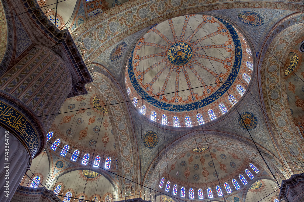 interior of the blue mosque in istanbul, with its colorful stained glass windows, its large arches, impressive ceiling with its central vault and large pillar in the foreground, Sultan Ahmed Mosque