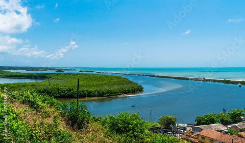 João de Tibas River that reaches the sea in Cabrália, seen from above with riparian forests, small boats and a beautiful blue sky with clouds