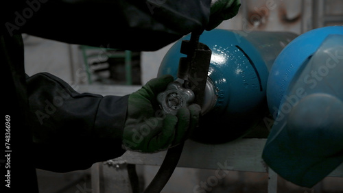 Close up of worker in gloves turning gas cylinder valve. Clip. Industrial background of the factory.