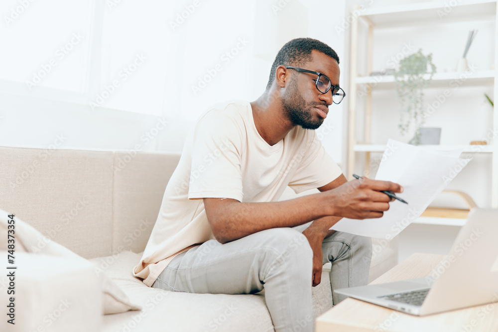 Smiling African American Freelancer Working on Laptop in Modern Living Room or Young African American Man Typing on Laptop, Enjoying His Freelance Job while Sitting on Sofa in Cozy Home